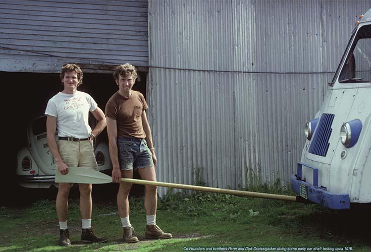 Grundarna av företaget står i shorts och tröja framför en bil och håller i en åra. Bild är tagen under 80-talet.